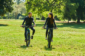 A blissful couple, adorned in professional cycling gear, enjoys a romantic bicycle ride through a park, surrounded by modern natural attractions, radiating love and happiness