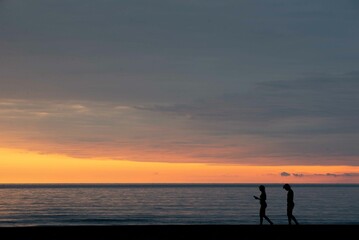 Fototapeta premium Two people walking on the shore at sunset