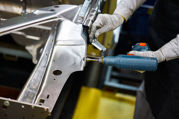 Worker prepares to screw car body parts on workshop conveyor