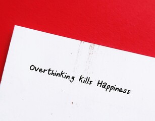 On red background, paper with handwritten text Overthinking kills happiness - to stop overthinking which magnifies problems and creates fear, doubt, regret and confusio