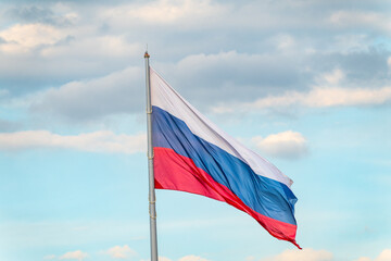 Russian tricolor flag waving in the wind against a blue sky.