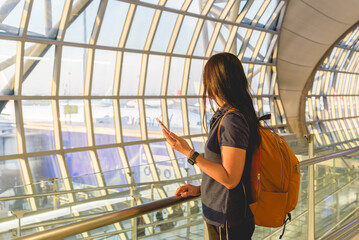 Casual female backpacker traveler at airport hold smart phone device while looking at the plane...
