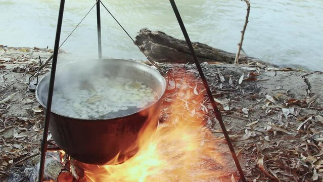 cook fish soup in a cauldron on a large fire in nature near the autumn river