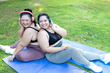 Cheerful laugh smiling friends young asian woman happy wear headphone listen to music in sportswear walking after exercise. Two sporty women body curvy positive having fun workout in garden.