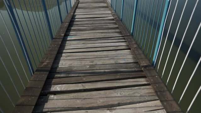 Camera moves forward revealing a narrow bridge with steel blue railings and suspenders over a murky body of water.