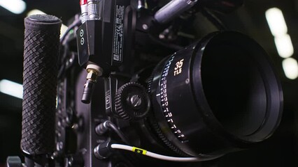 Modular professional cinema camera with sensor block separated from the body, high end cinema lens focus ring being turned by a remote focus motor by a focus puller. Low angle studio setting.