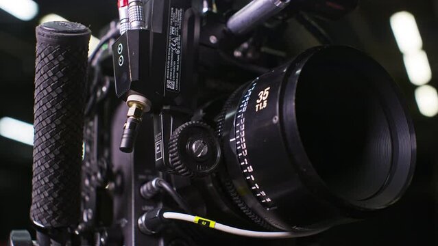 Modular professional cinema camera with sensor block separated from the body, high end cinema lens focus ring being turned by a remote focus motor by a focus puller. Low angle studio setting.