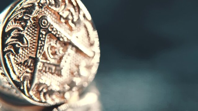 A macro detailed tilt down shot of a golden textured freemasons ring, on a rotating stand, mirror reflection, illuminati symbol, professional studio lighting, 4K video