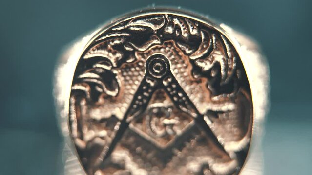 A macro detailed smooth tilt up shot of a golden textured freemasons ring, on a reflecting stand, illuminati symbol, professional studio lighting, 4K video