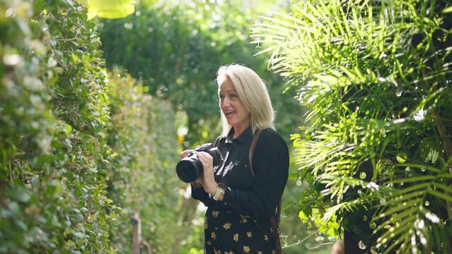 Blonde Photographer With DSLR Camera Posing Subjects For Outdoor Photo Shoot In Green Garden, 4K Resolution Slow Motion