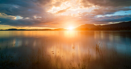 A peaceful waterfront with serene reflections under a bright, sunny sky.
