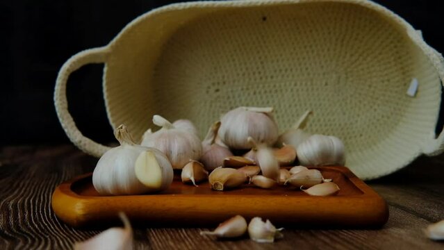 Garlic cloves falling on a wooden plate surrounded by garlic