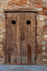 Old, wooden, textured door on aging brick building in Tuscany, Italy