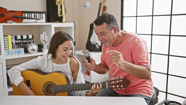 Classic melody in unison, smiling man and woman musicians, confidently playing acoustic guitar, singing soulful song together at spanish music studio