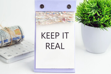 KEEP IT REAL text, word, inscription on a desktop calendar on a white background next to money and a green flower