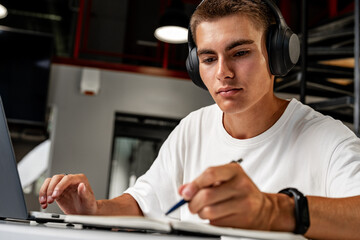 Young man wearing headphones while studying with laptop