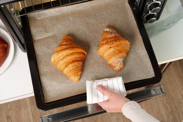 Female hand taking delicious croissants out of electric oven in kitchen