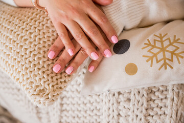 Female hand with beautiful natural manicure - pink nude nails on pale beige fluffy fabric, textile background. winter holidays outfit.fashionable pink manicure