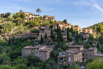 Fototapeta na wymiar Stunning cityscape of the small coastal village Deia in Mallorca, Spain. Traditional houses located in terraces on the hills surrounded by green trees. Spanish tourist destinations.