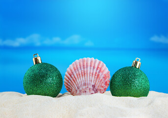 Pink conch with Christmas shiny green balls on sand of beach with sea. New Year, holiday. Copy space