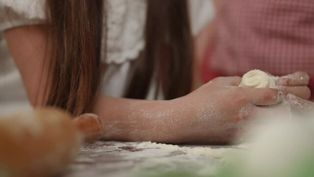 Slow motion. Close-up. Cooking with mom. Mom helps her daughter with the dough rolled into a roll