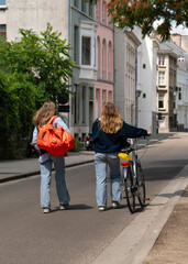 Back rear view of two blondes, one pushing a bicycle. Ghent, Belgium.