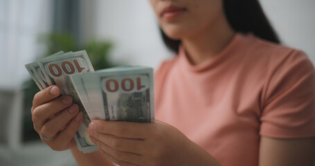 Portrait of Happy young asian woman counts cash dollar bills while sitting in living room at...