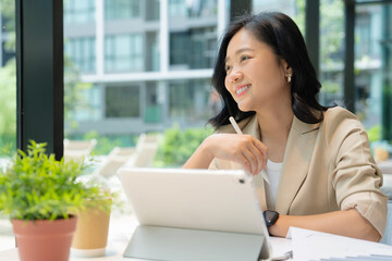 Happy Asian businesswoman working with laptop and documents on table in coffee shop