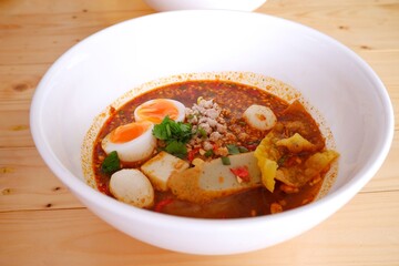 Delicious Tom Yum noodles with eggs ready to eat on white bowl on wooden table background.