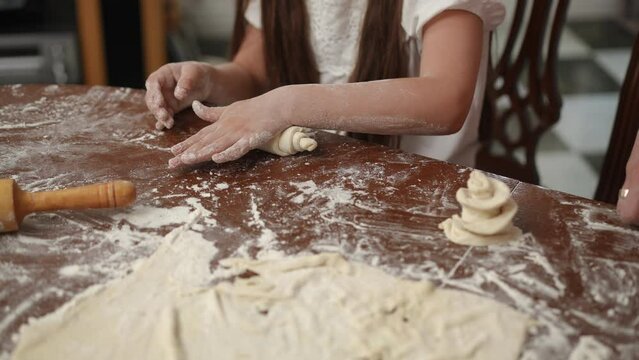 Family leisure time in the home kitchen in a modern house. The daughter learns to work with rolled out dough under the guidance of her mother