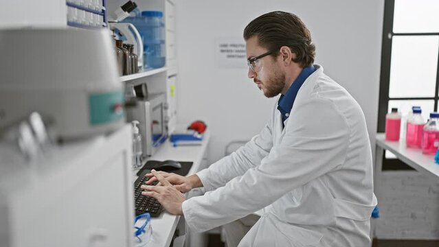 Young hispanic man scientist using computer taking glasses off stretching arms at laboratory