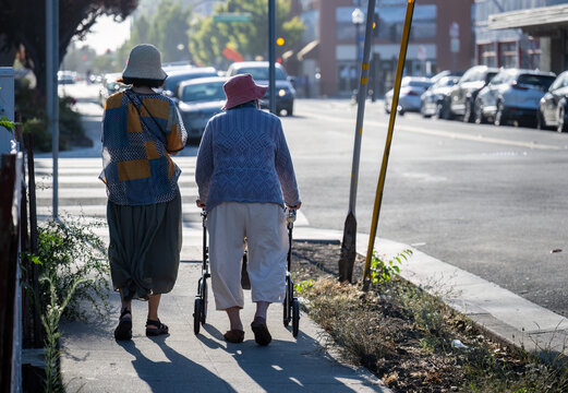 Senior woman walking using a mobility walker on the pedestrian walkway in the city, accompanied by her daughter.