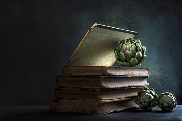 The artichokes are on the book. Artichokes and an old book. Dark background. An old book. Copy...