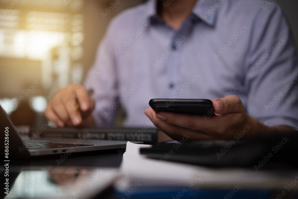 Wall mural businessman hand holding mobile smartphone on a table with a laptop at office...