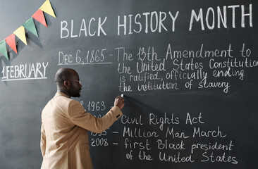 African American teacher writing information about Black History Month on blackboard during a lesson