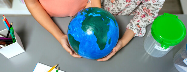 Top view of two unrecognizable female students holding in their hands a handmade globe world earth...
