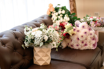 Several bouquets of flowers lie on a brown sofa near the window. Gifts from guests at the holiday.