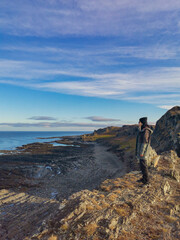 A woman on the background of the rocky coast of the Barents Sea. Beautiful view of the cliffs and the coast of the Rybachy and Sredny peninsulas. The harsh beauty of the north.