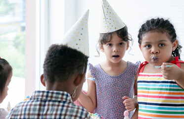 Group of multiracial children friends wear hat enjoy eating rainbow cake, sugar candies and jelly...