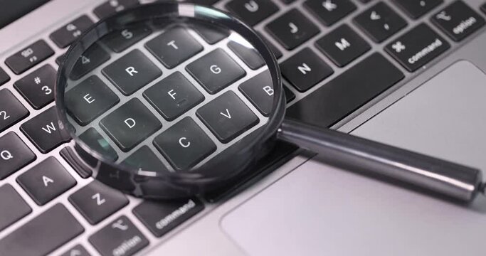 Magnifying glass lying on laptop keyboard 4k movie slow motion. Programming concept