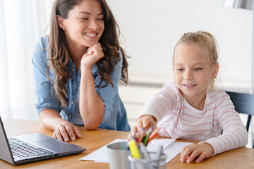 Mother and daughter learning together at home, sitting at the desk in front of a computer. Back to school