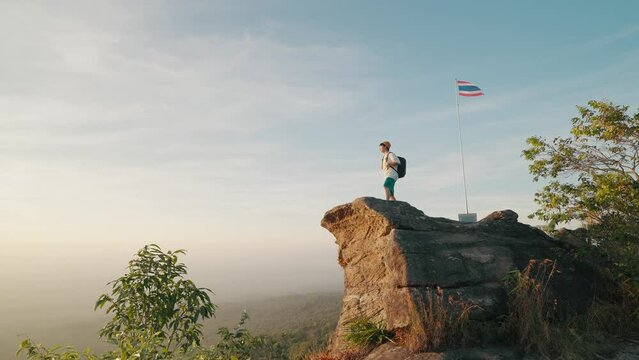 A man backpacker traveling alone standing on the big rock mountain at Pha Chu Thong in Phu Hin Rong Kla National Park Thailand. Successful man enjoying triumph. Travel on top of high rock concept