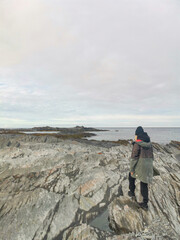 Fototapeta premium A woman on the background of the rocky coast of the Barents Sea. Beautiful view of the cliffs and the coast of the Rybachy and Sredny peninsulas. The harsh beauty of the north.