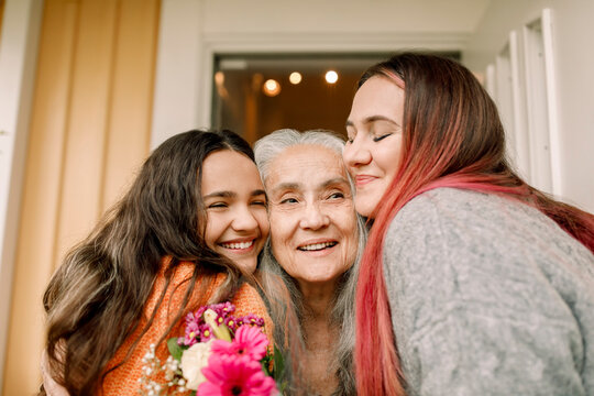 Cheerful senior woman greeting daughter and granddaughter in front of doorway