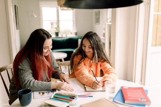 Happy woman assisting daughter in homework while sitting at table