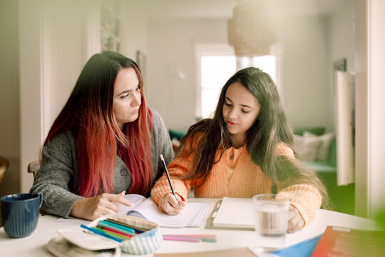 Woman assisting daughter in doing homework while sitting at table