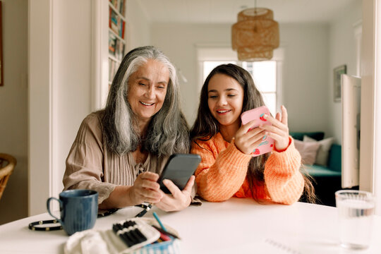 Happy grandmother and granddaughter using smart phone at home
