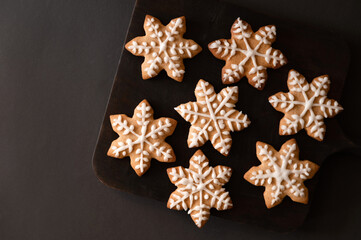 Obraz na płótnie Canvas Snowflake shape gingerbread sugar cookie decorated with icing on black wooden board, on dark table background. Traditional Christmas baked dessert. Flat lay, copy space
