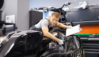 Male mechanic diagnoses modern motorcycle in service center. Concept of vehicle maintenance and...