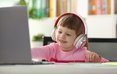 Portrait of a little child girl in headphones with laptop. Watching cartoons and kids remote learning concept